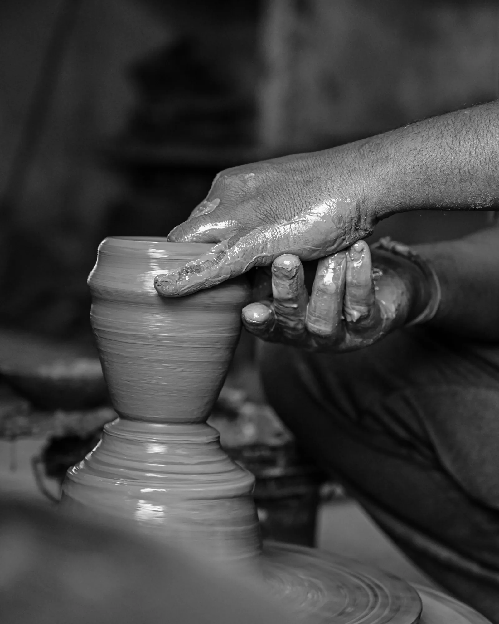Wet clay rising between two hands on a spinning potter's wheel, in black and white