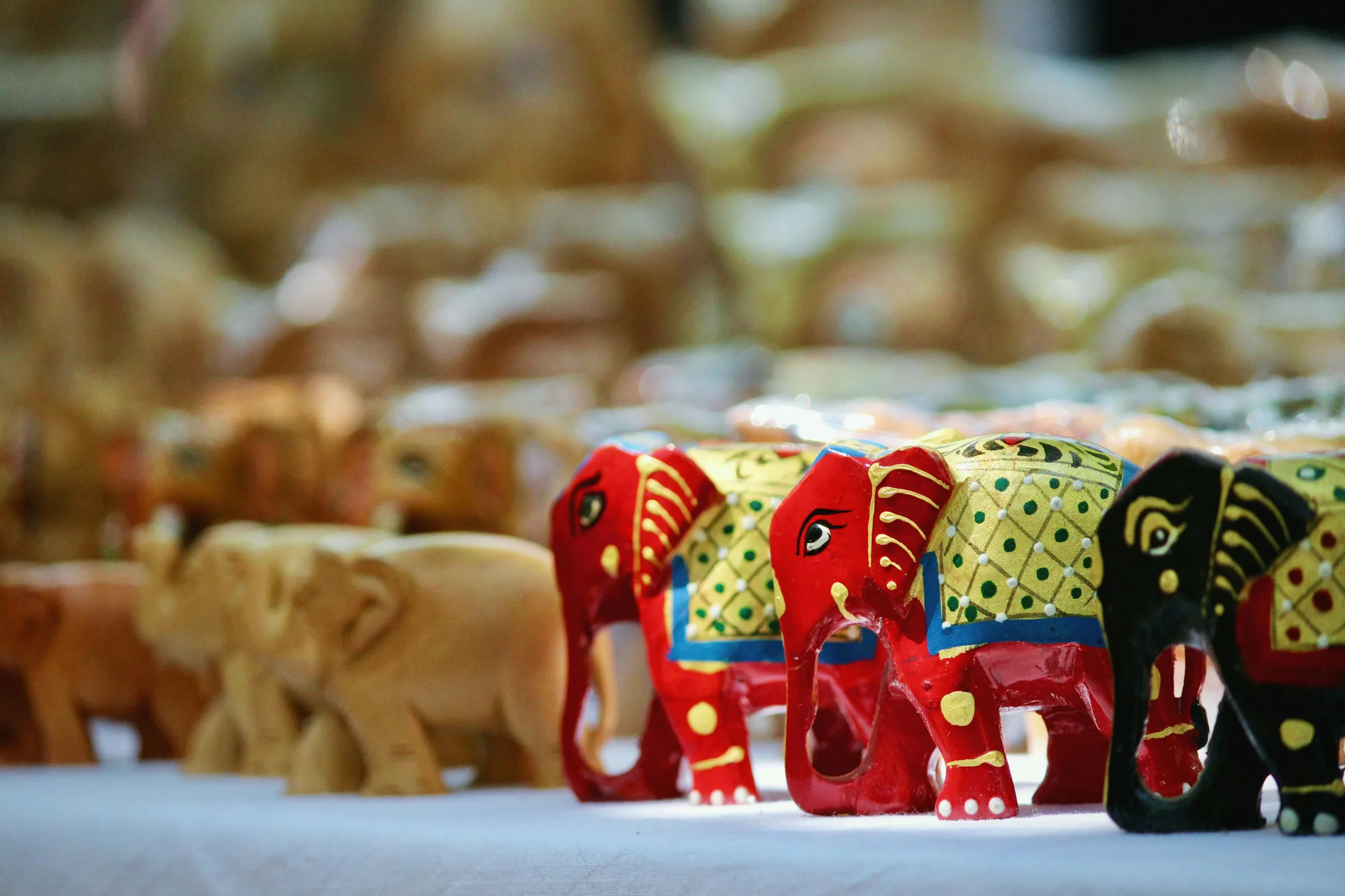A row of small carved elephants, some painted in red and green, some left as bare wood