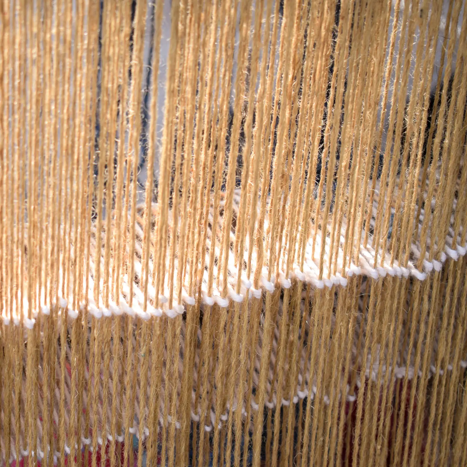 Pale natural-fibre warp threads stretched on a loom, crossed by stepped rows of white weft