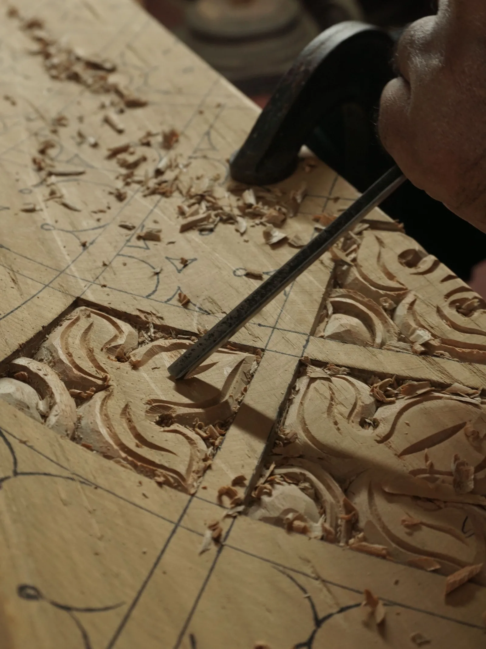 A chisel and mallet resting on a panel carved with deep scrolling leaves, shavings scattered across it